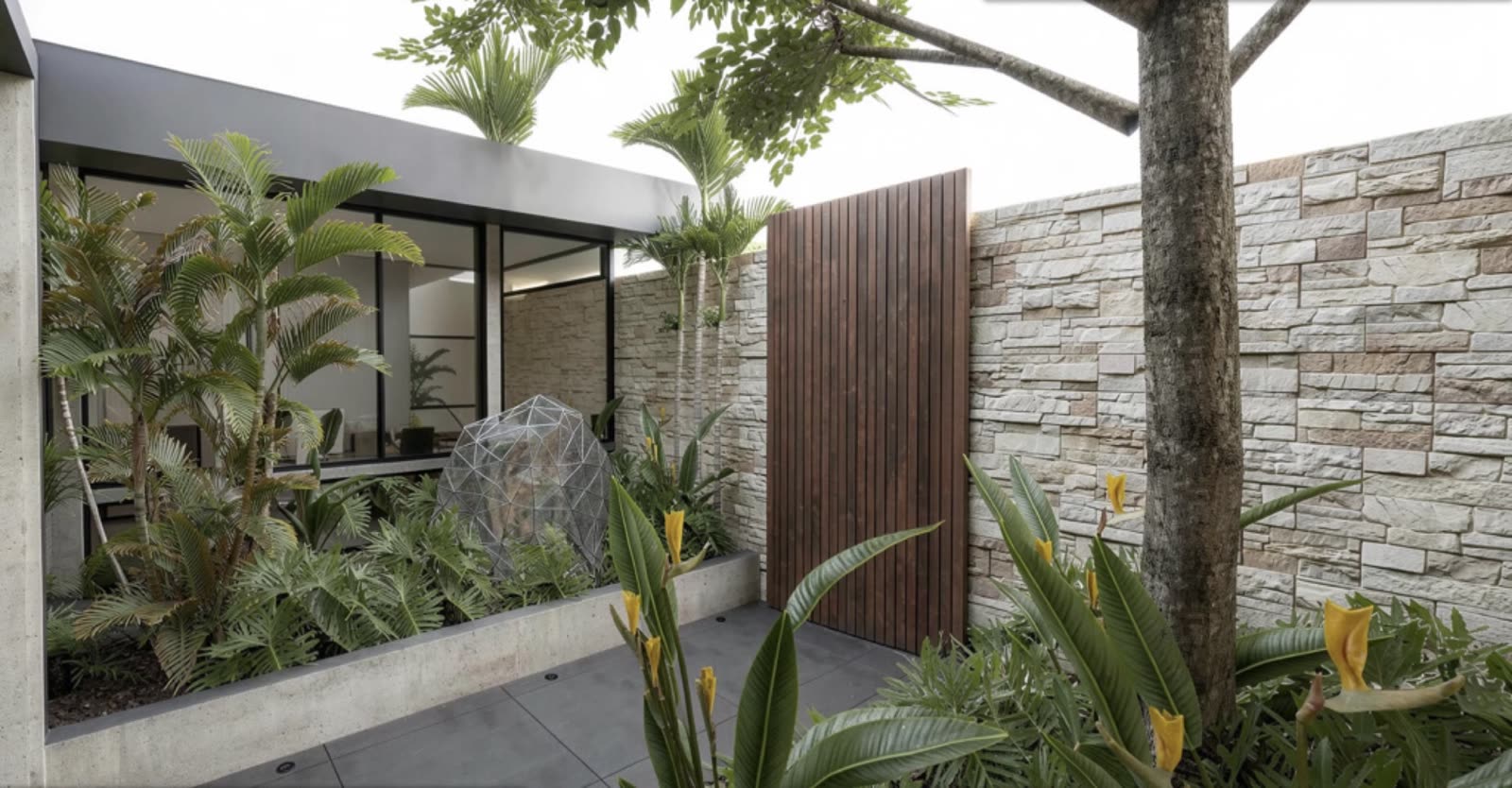 Interior courtyard garden with tropical planting and a wood-slat gate against a stone wall