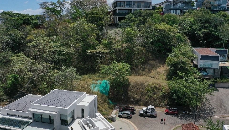 Vista con dron del lote desde la calle, entre casas modernas terminadas